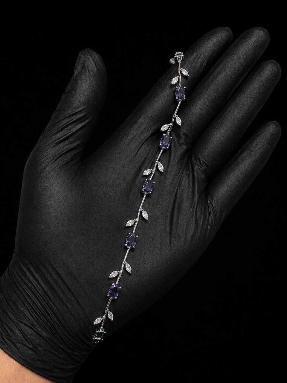 A silver vine bracelet with purple gemstones and clear crystal leaves, displayed on a hand wearing a black glove against a black background.