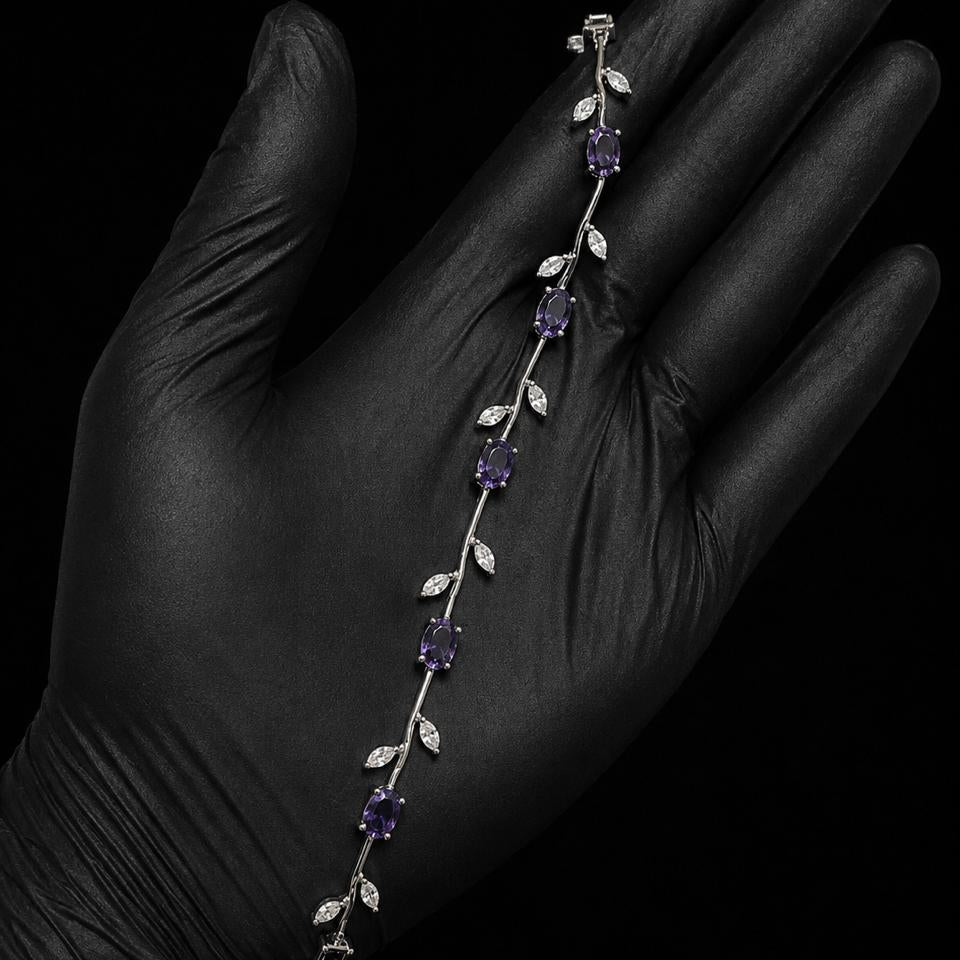 A silver vine bracelet with purple gemstones and clear crystal leaves, displayed on a hand wearing a black glove against a black background.