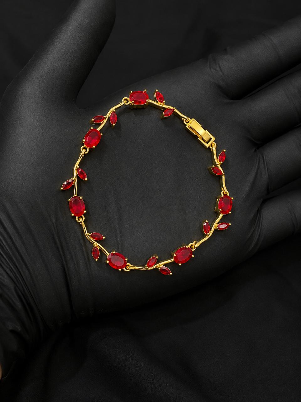 A gold bracelet with red marquise and oval gemstones, displayed on a black gloved hand.
