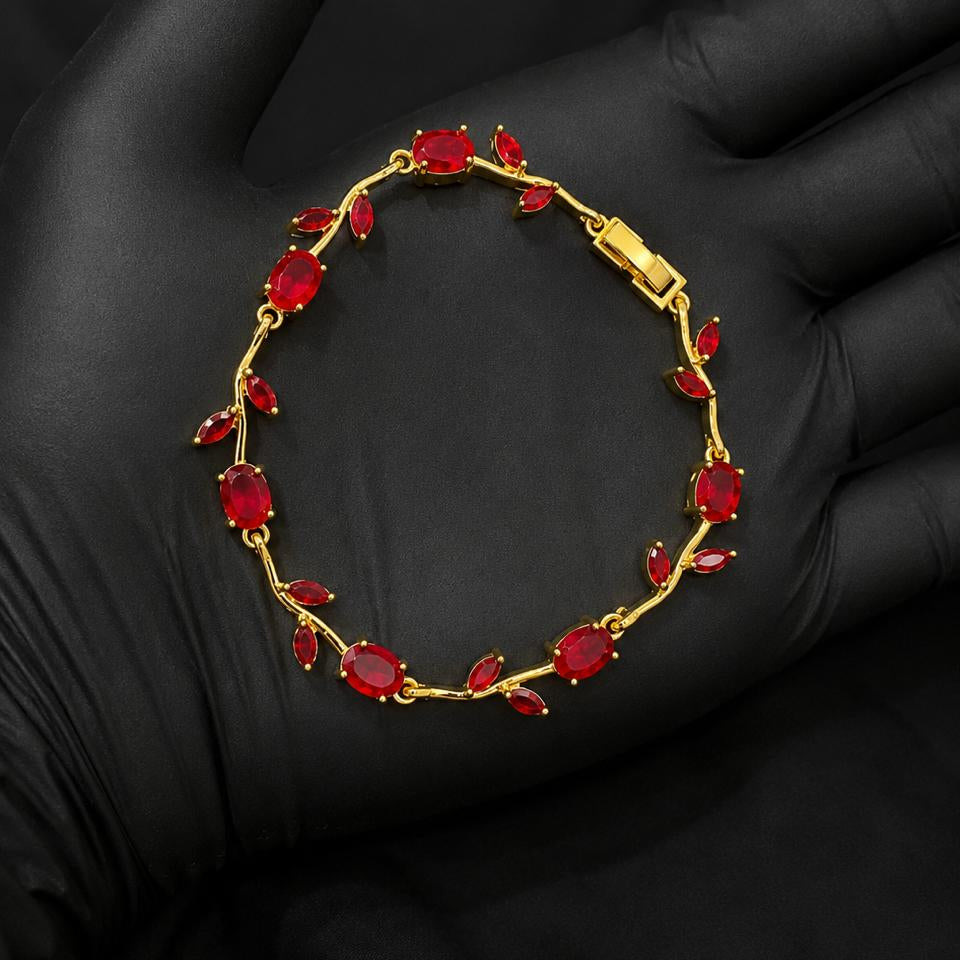 A gold bracelet with red marquise and oval gemstones, displayed on a black gloved hand.