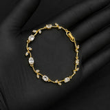 A delicate gold bracelet with clear gemstones arranged in a vine pattern, displayed on a black gloved hand against a dark background.