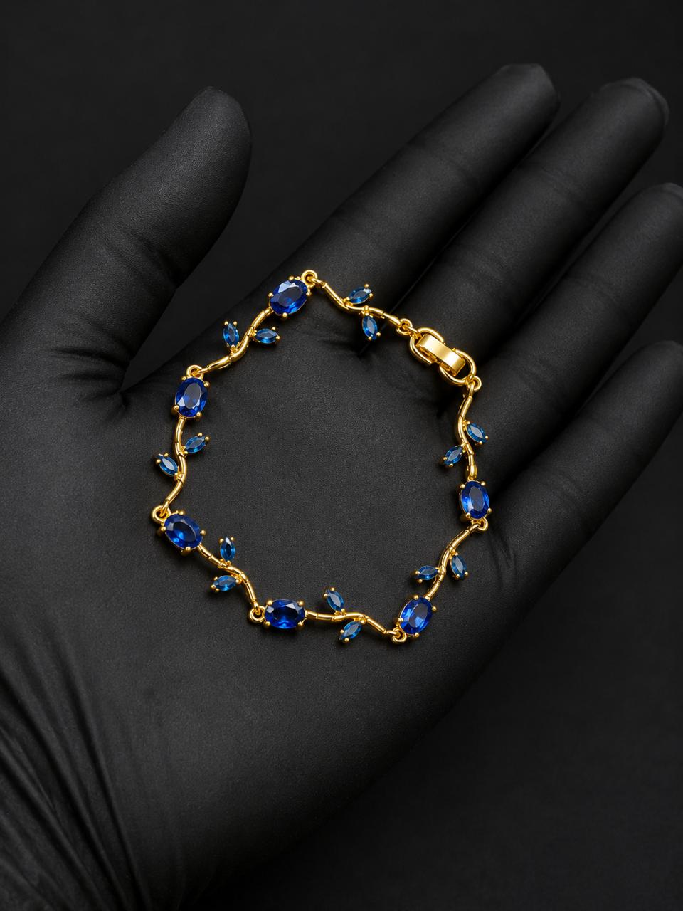 A gold bracelet with blue gemstones, displayed on a black gloved hand against a dark background.