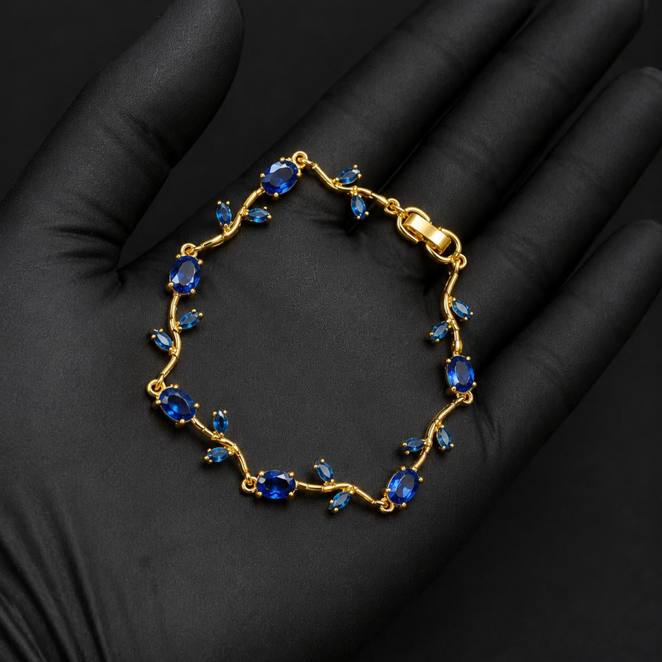 A gold bracelet with blue gemstones, displayed on a black gloved hand against a dark background.