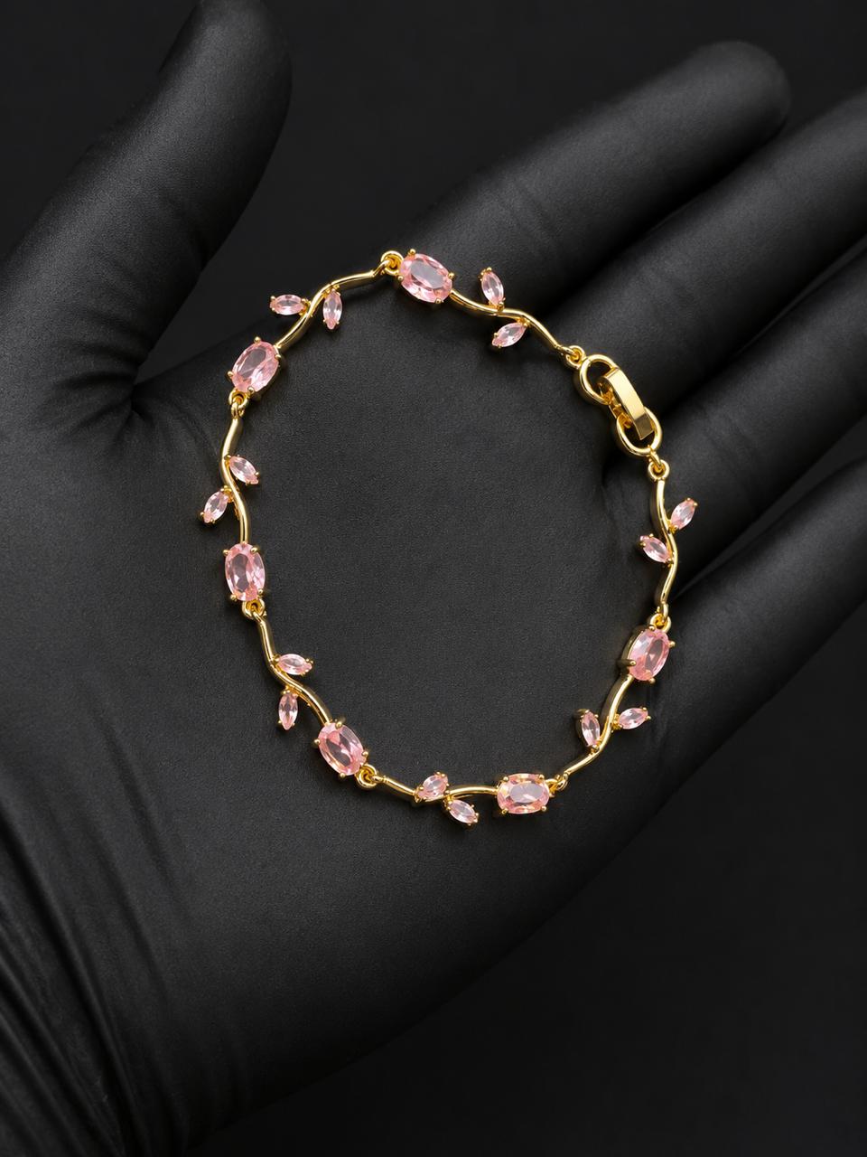 A delicate gold bracelet with small pink marquise-cut stones, displayed on a black gloved hand.