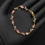 A delicate gold bracelet with small pink marquise-cut stones, displayed on a black gloved hand.