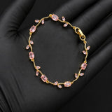 A delicate gold bracelet with small pink marquise-cut stones, displayed on a black gloved hand.