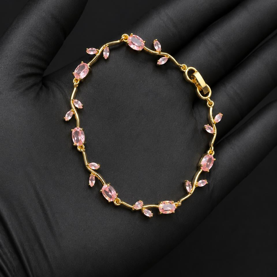 A delicate gold bracelet with small pink marquise-cut stones, displayed on a black gloved hand.