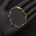 A gold bracelet with red oval gemstones and small green leaf accents, displayed on a black gloved hand.