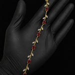A gold vine-style bracelet with red gemstones and clear stones, displayed on a hand wearing a black glove against a black background.