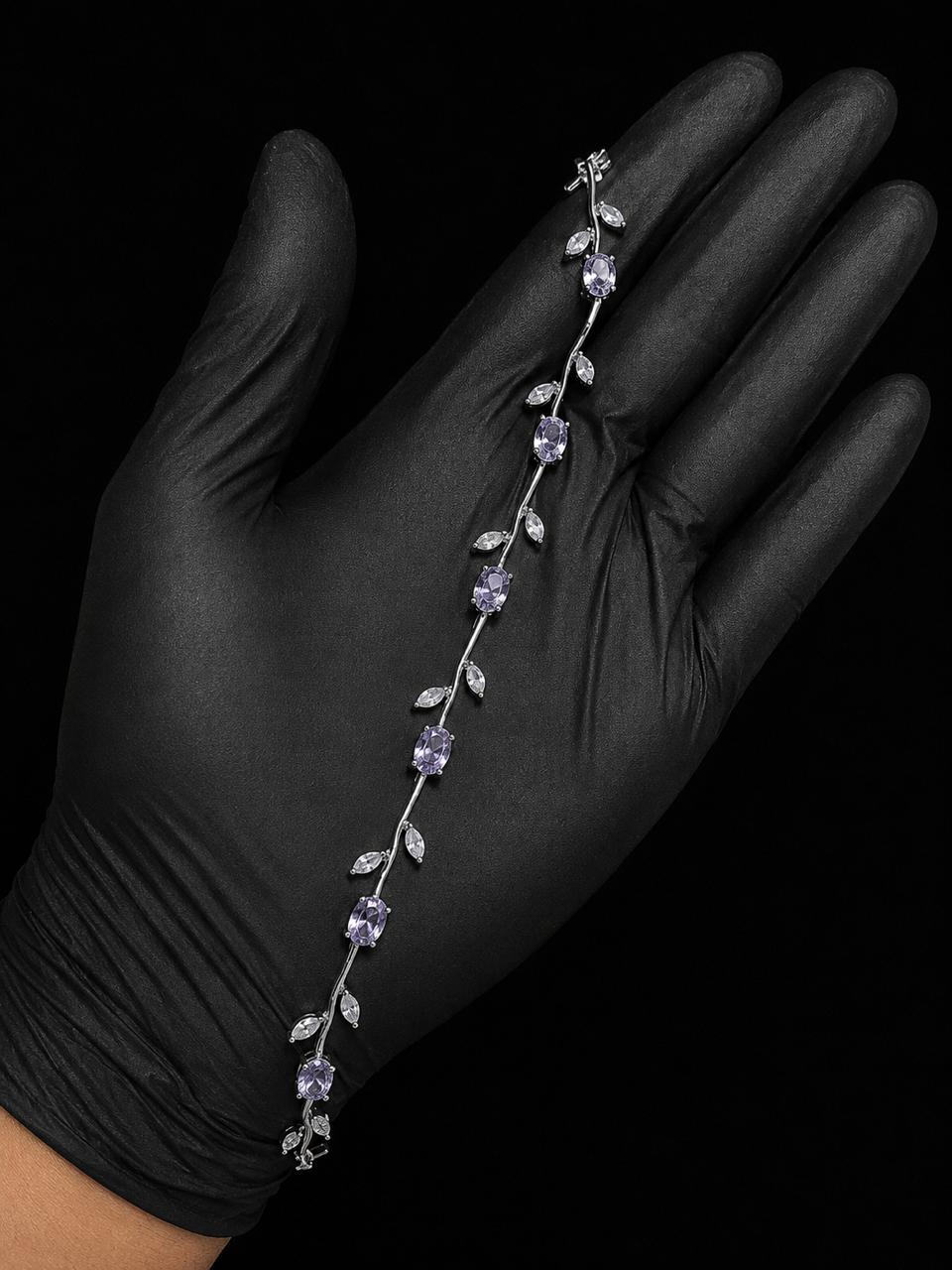 A silver vine-style bracelet with white gemstones and clear accent stones, displayed on a hand wearing a black glove against a black background.