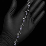A silver vine-style bracelet with white gemstones and clear accent stones, displayed on a hand wearing a black glove against a black background.