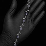 A silver vine-style bracelet with white gemstones and clear accent stones, displayed on a hand wearing a black glove against a black background.