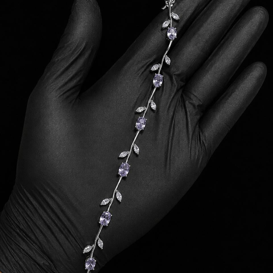 A silver vine-style bracelet with white gemstones and clear accent stones, displayed on a hand wearing a black glove against a black background.