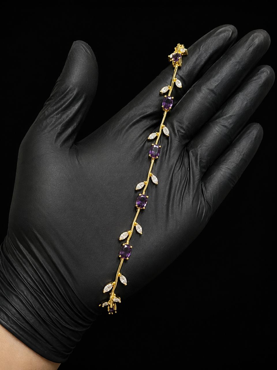 A gold vine-style headband with purple amethyst gemstones and white crystal leaves, held in a hand wearing a black glove against a black background.