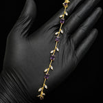 A gold vine-style headband with purple amethyst gemstones and white crystal leaves, held in a hand wearing a black glove against a black background.
