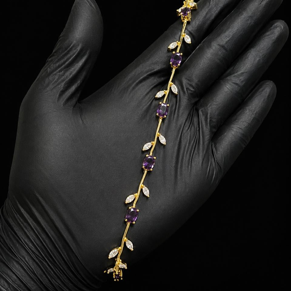 A gold vine-style headband with purple amethyst gemstones and white crystal leaves, held in a hand wearing a black glove against a black background.